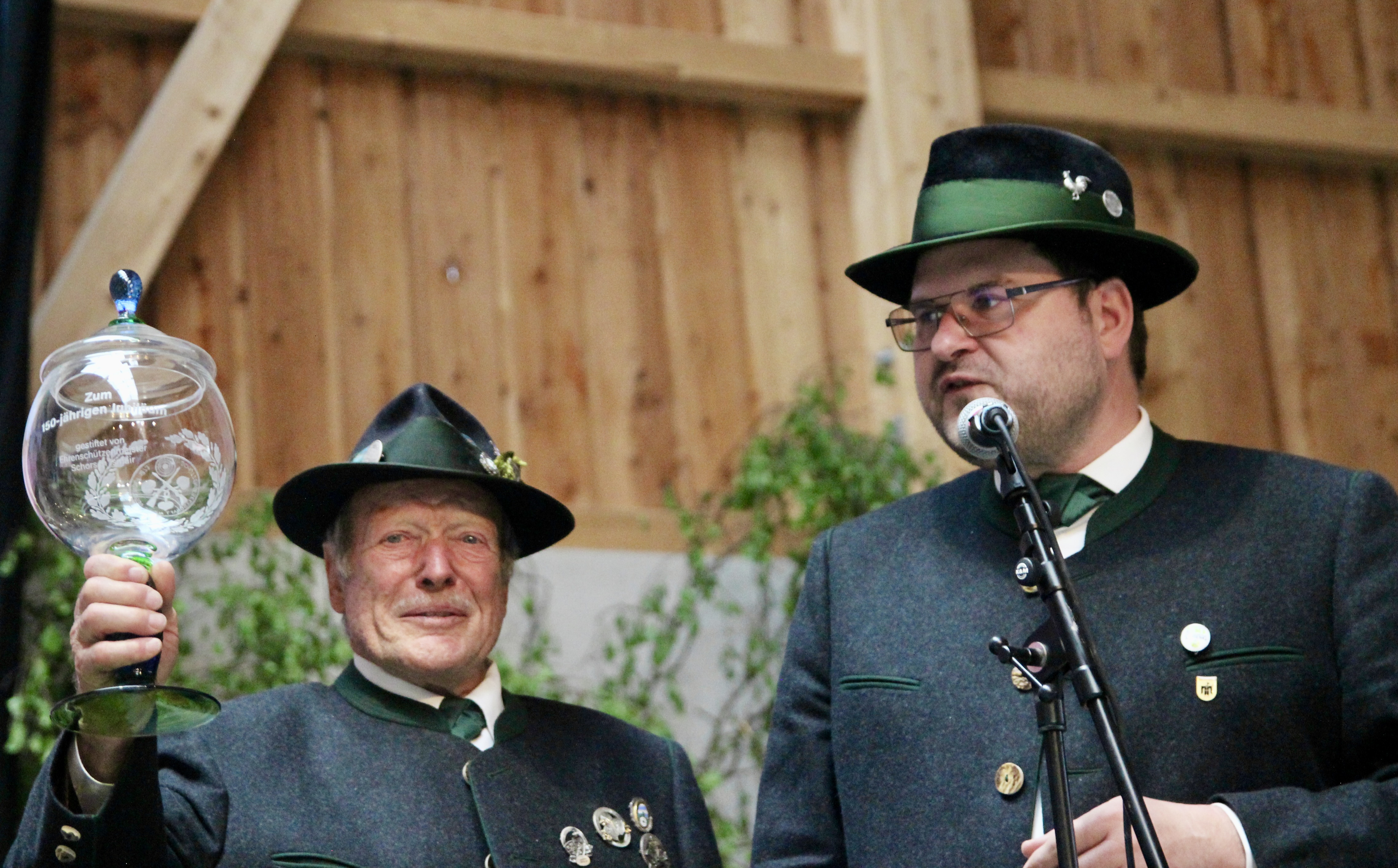 Der Aubinger Ehrenschützenmeister Georg Ismair stiftete einen großen gläsernen Jubiläumspokal sowie fünf kleinere, die die Schützen erhielten, die beim Jubiläumsschießen am nächsten an 150 Teiler lagen. Rechts Moderator Sebastian Kriesel.