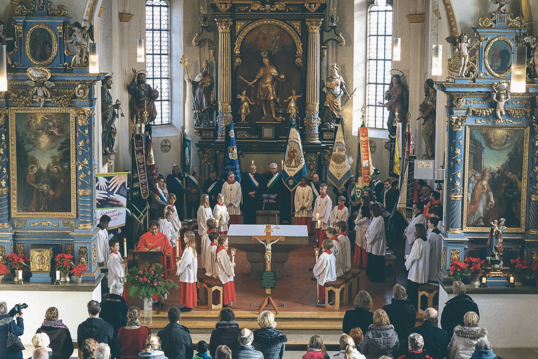Das Kreuz mit der Gedenktafel vor dem Altar in der Pfarrkirche erinnert an die Choleraepidemie im Jahr 1854. Die Fahnenabordnungen der Vereine sammeln sich zur Feier im Halbrund um den Altar.